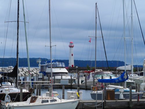 A marina with various boats and a red and white lighthouse in the background under a cloudy sky.