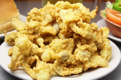 A plate piled high with golden, crispy fried food, surrounded by a side of salad and bread.