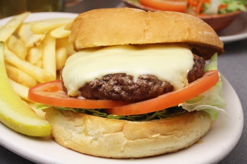 A juicy cheeseburger with melted cheese, lettuce, and tomato, served with fries and a pickle on the side.