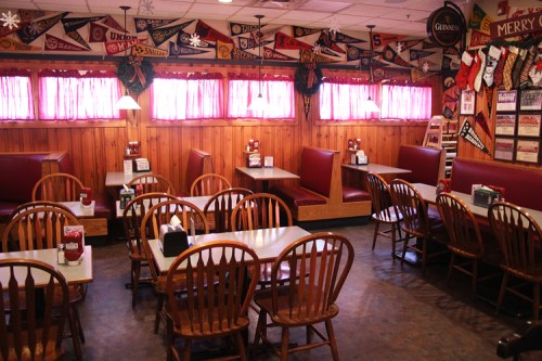 Cozy restaurant interior with wooden booths, tables, and colorful banners hanging on the walls. Warm, inviting atmosphere.