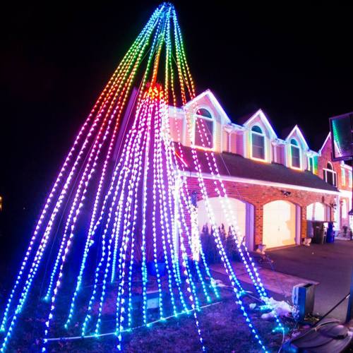 A house decorated with colorful LED lights, featuring a tall, illuminated tree design in the front yard.