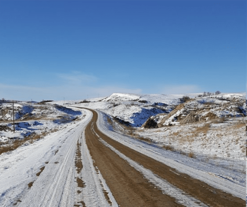A winding dirt road through a snowy landscape under a clear blue sky.