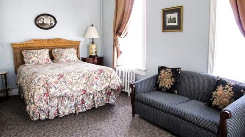 Cozy bedroom with a floral bedspread, a sofa, and natural light from large windows.