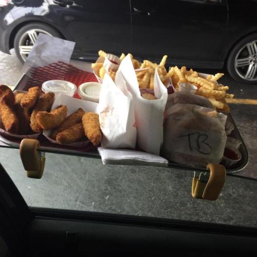 A tray of fast food with chicken strips, fries, and dipping sauces, resting on a car window.