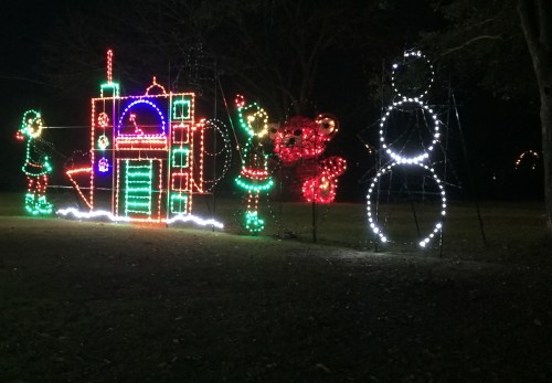 Colorful holiday lights display featuring a festive scene with a snowman, elves, and a decorated structure.