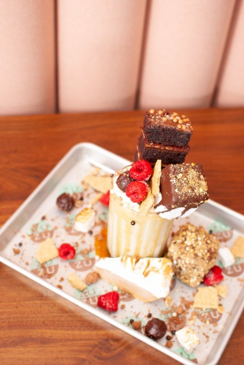 A tall milkshake topped with brownies, raspberries, chocolate, and graham crackers on a tray.