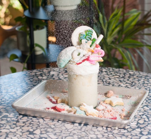 A whimsical milkshake topped with colorful candies and whipped cream, surrounded by sprinkles on a patterned table.