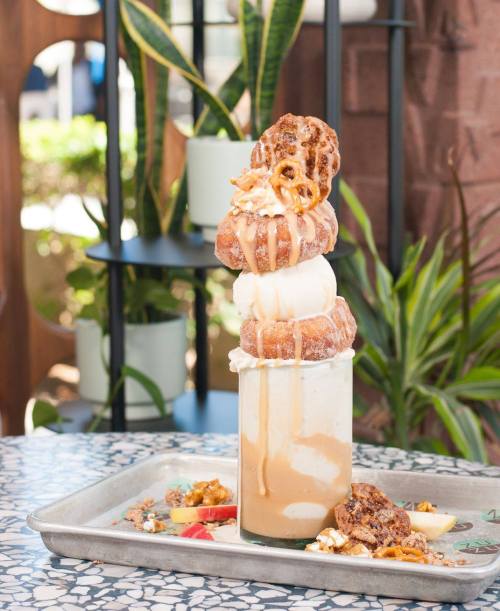 A tall dessert featuring ice cream, cookies, and pretzels drizzled with caramel, served in a glass on a tray.