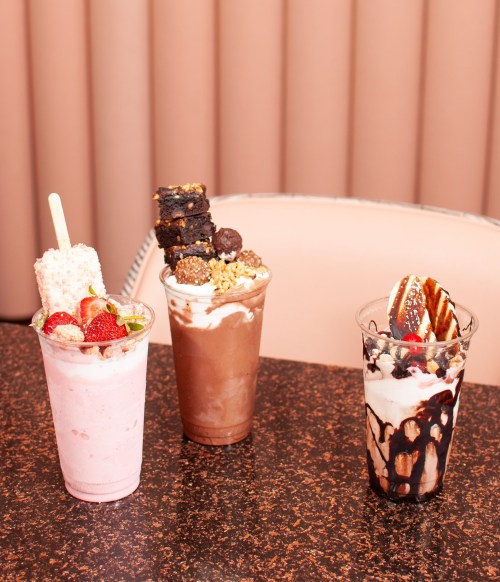 Three colorful dessert drinks on a table: a strawberry shake, a chocolate shake with toppings, and a layered sundae.