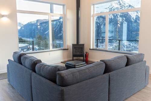 Cozy living room with a gray sectional sofa, a wood stove, and large windows showcasing a mountain view.