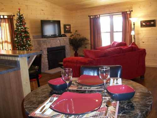 Cozy cabin interior with a dining table set, a red couch, a Christmas tree, and a stone fireplace.