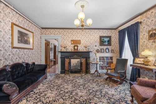 Cozy vintage living room with floral wallpaper, a fireplace, and antique furniture, featuring a patterned rug and warm lighting.