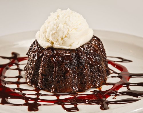 A rich chocolate dessert topped with a scoop of vanilla ice cream, drizzled with chocolate sauce on a white plate.