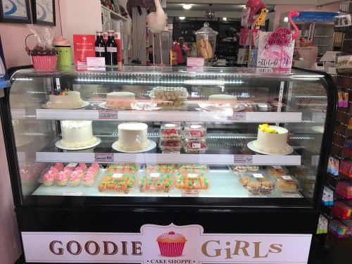 Display case at a bakery featuring various cakes, cupcakes, and desserts with colorful decorations.