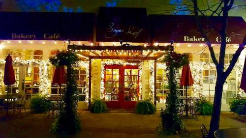 A cozy bakery café adorned with festive lights and greenery, featuring outdoor seating and a welcoming entrance.