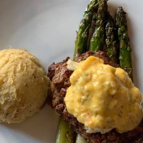 A plate featuring grilled asparagus, a meat patty topped with creamy sauce, and a scoop of mashed potatoes.
