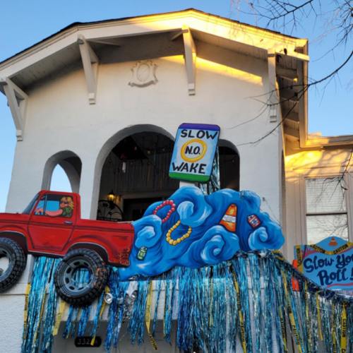 A colorful mural on a building featuring a red truck and waves, with signs reading "Slow No Wake" and "Slow Your Roll."