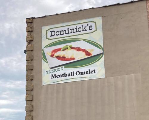 Sign for Dominick's featuring a meatball omelet with sauce, set against a cloudy sky.