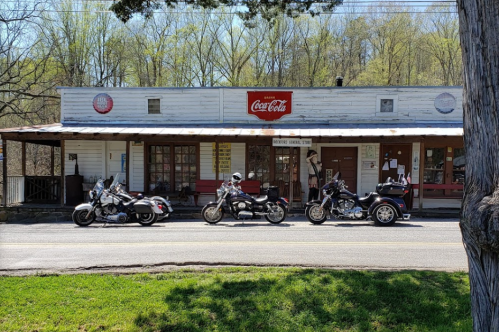A row of motorcycles parked in front of a vintage store with a Coca-Cola sign and a rustic wooden facade.