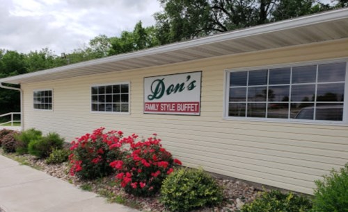 Exterior of Don's Family Style Buffet, featuring a light-colored building and blooming flowers in front.