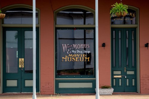 Exterior of a building featuring a sign for "Willie Morris & My Dog Skip Movie Museum" with green doors and windows.