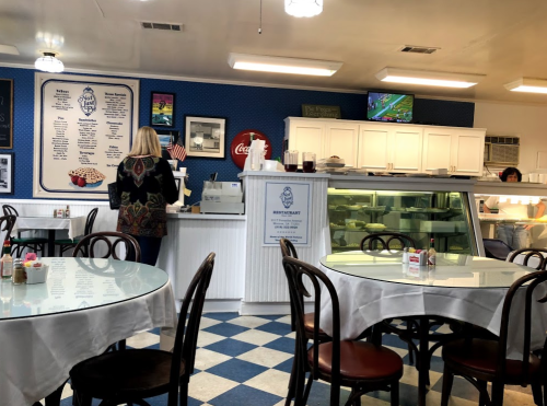 A cozy diner interior with checkered floors, tables set for dining, and a counter with a menu and ice cream display.