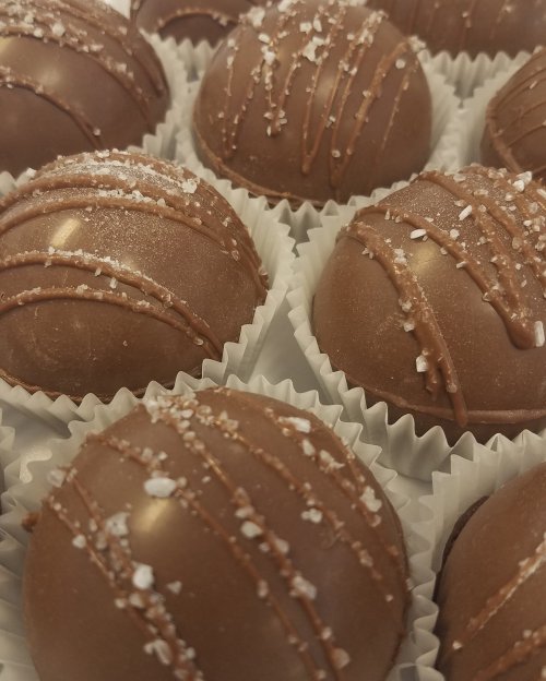 Close-up of chocolate truffles with a glossy finish, drizzled with chocolate and sprinkled with sea salt.