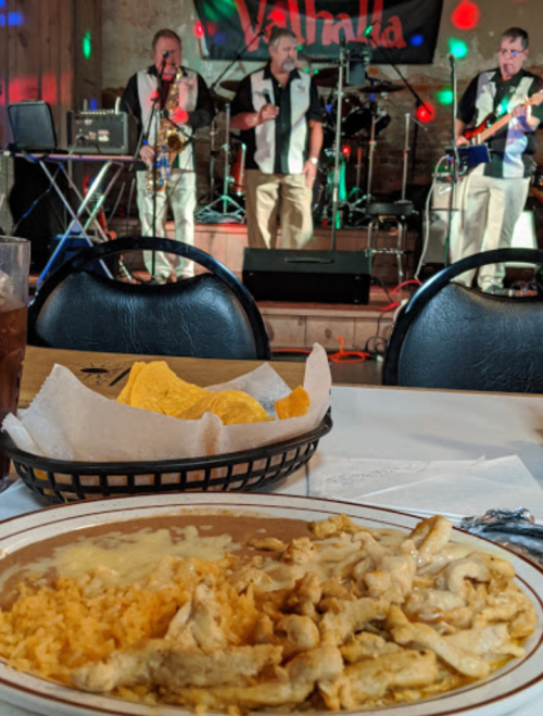 A plate of food with rice and chicken in the foreground, while a live band performs in the background.