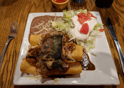 A plate of enchiladas topped with sauce, served with refried beans and a side salad of lettuce, tomatoes, and sour cream.