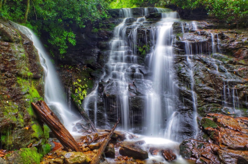 A serene waterfall cascading over rocky terrain, surrounded by lush greenery and moss-covered stones.