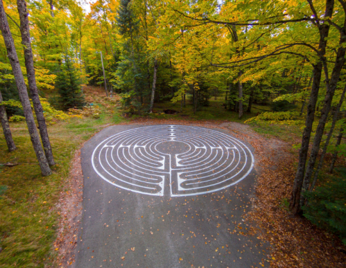 Aerial view of a circular maze on a forest path, surrounded by colorful autumn foliage.