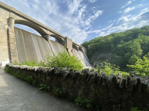 A large dam with water cascading down, surrounded by lush greenery and a stone pathway in the foreground.