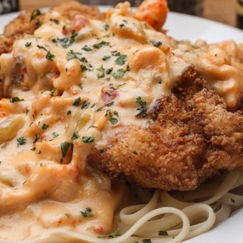 A plate of fried chicken topped with creamy shrimp sauce, served over a bed of spaghetti and garnished with parsley.