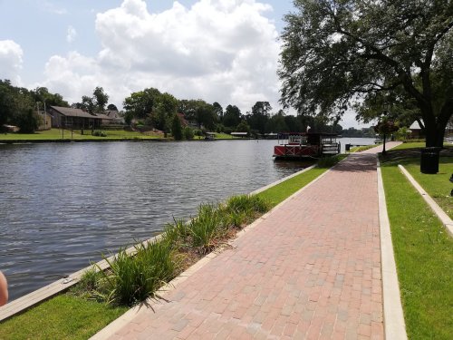 A peaceful riverside path lined with grass and plants, leading to a calm waterway with a boat docked nearby.