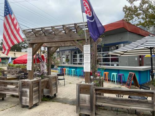 A colorful outdoor dining area with wooden seating, flags, and a vibrant bar in a casual restaurant setting.