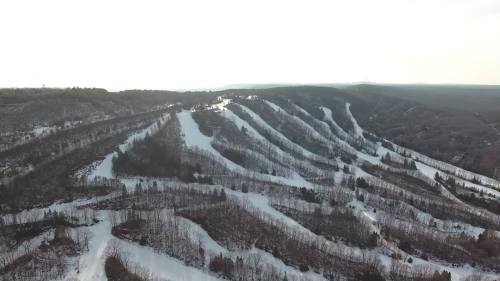Aerial view of snow-covered ski slopes winding through a forested landscape under a clear sky.