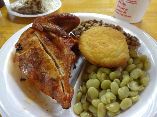 A plate of food featuring grilled chicken, cornbread, black-eyed peas, and lima beans on a white disposable plate.
