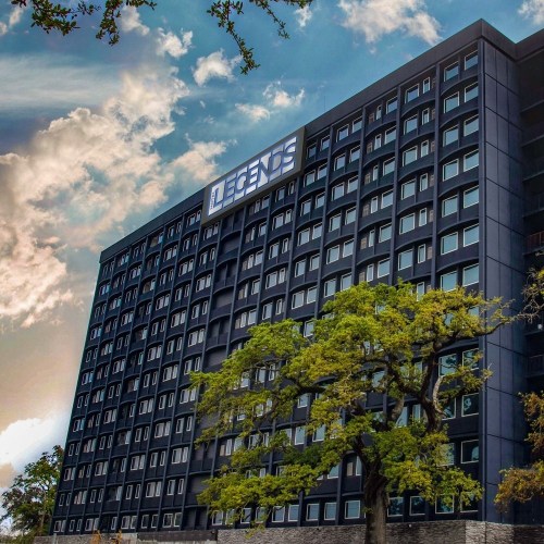 A tall, modern building with the sign "LEGENDS" on top, surrounded by trees and a cloudy sky.