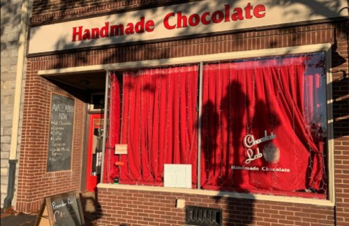 A storefront with a red curtain, sign reading "Handmade Chocolate," and a chalkboard menu outside.