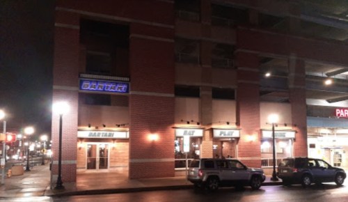 Exterior of a brick building at night, featuring a sign for "BANTAI" and nearby parking structure.