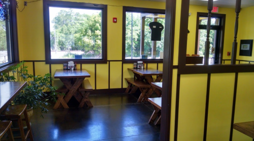 Brightly lit restaurant interior with yellow walls, wooden tables, and large windows overlooking greenery.