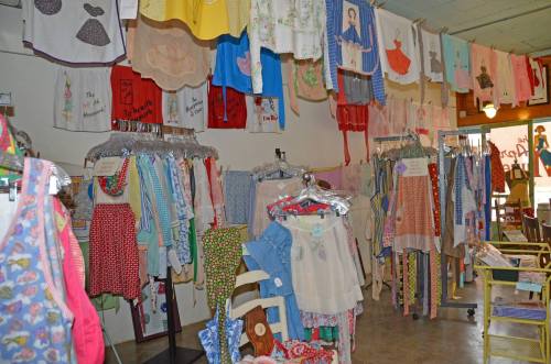 A colorful display of vintage aprons and clothing hanging on racks and walls in a charming shop.