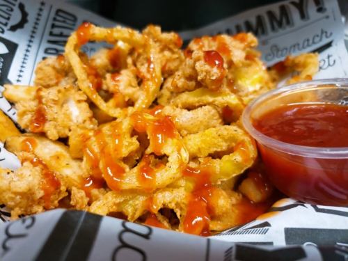 A close-up of crispy fried onion rings drizzled with sauce, served with a side of dipping sauce in a paper-lined basket.