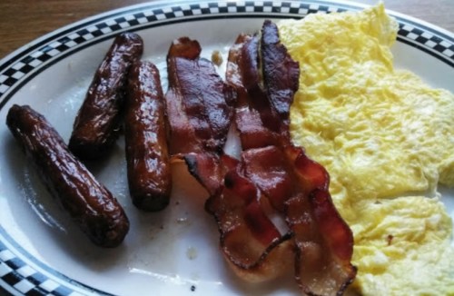 A plate with scrambled eggs, crispy bacon, and grilled sausages.