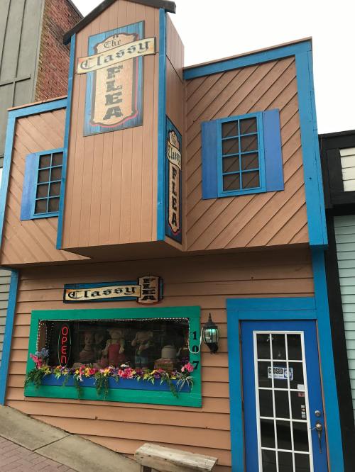 A colorful building with a sign reading "The Classy Flea," featuring a flower-adorned window and an open sign.