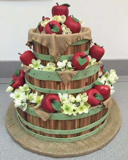A three-tiered cake designed to look like wooden barrels, topped with red apples and white flowers.