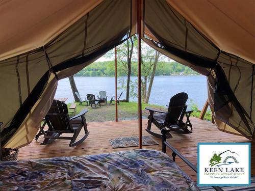 View from a tent overlooking a lake, with two rocking chairs on a wooden deck and trees in the background.
