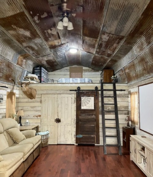 Cozy interior of a rustic room with a loft, wooden walls, a sofa, and a ladder leading to the upper sleeping area.