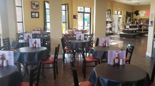 Interior of a restaurant featuring empty tables with black tablecloths, menus, and ketchup bottles on each table.
