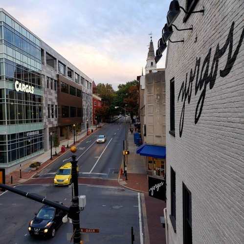 View of a city street with shops, a Starbucks, and a church steeple in the background, captured from a building.